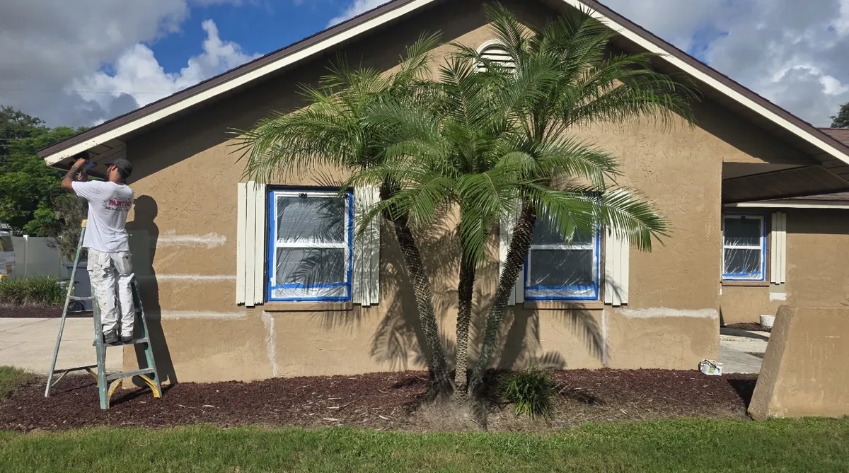 John Crouthers Painting crew member on a ladder masking windows and prepping a stucco home for exterior painting in Lakeland FL